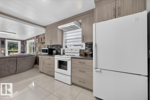 Kitchen with light brown cabinets, white appliances, white oven, and a dishwasher, adjacent to living area. - 163041 Town Ship 565, Rural Lamont County