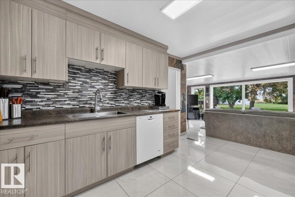 Kitchen with light wood cabinets, stainless steel sink, dishwasher, and large windows overlooking the yard. - 163041 Town Ship 565, Rural Lamont County