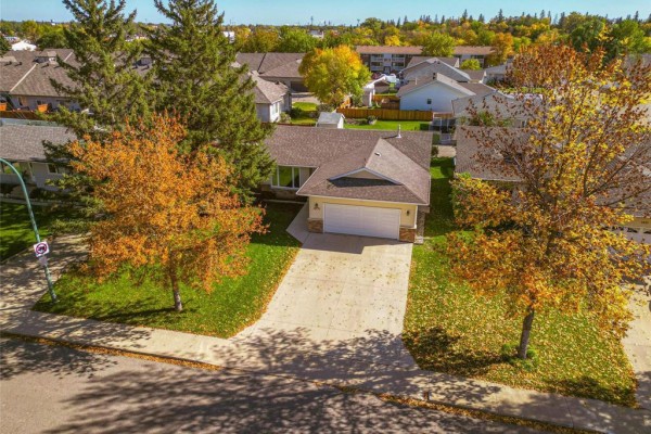 Aerial view of the beige bungalow with a driveway surrounded by fall foliage. - 1631 22nd Street, Brandon