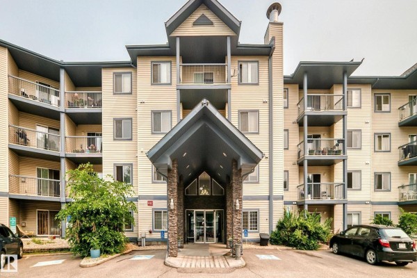Exterior view of a beige apartment building with multiple balconies and a central covered entrance. - #138 16311 95 St Nw, Edmonton