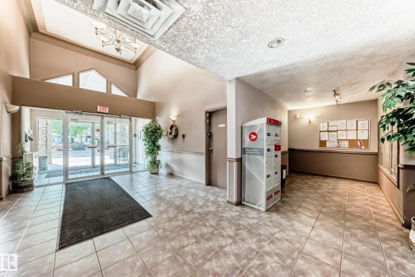 Apartment building lobby with tiled floors, mailboxes, and a bulletin board near the entrance. - #138 16311 95 St Nw, Edmonton
