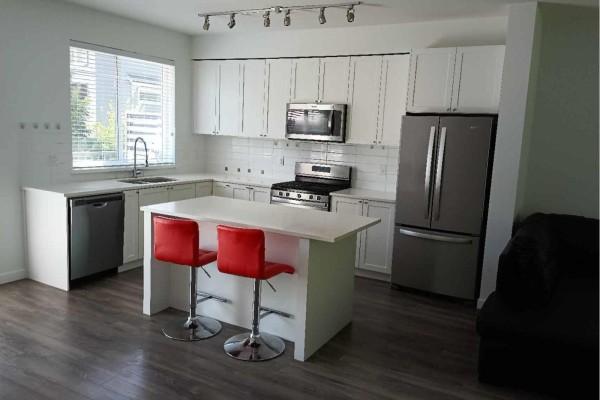 Kitchen with white cabinets, stainless steel appliances, island, and red stools. - 16337 15 Avenue, Surrey