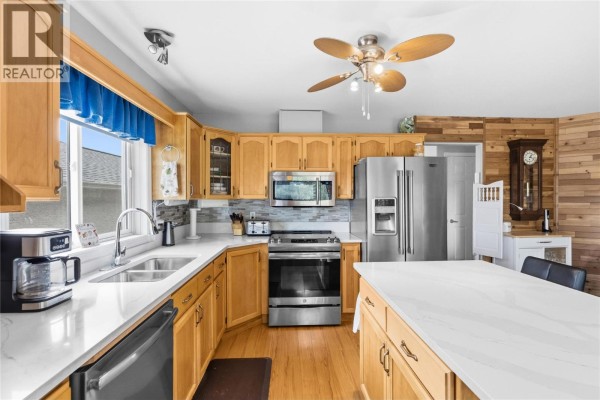 Kitchen with light wood cabinets, stainless steel appliances, white quartz countertops, and a large island. - 1634 Carmi Avenue Unit# 121, Penticton