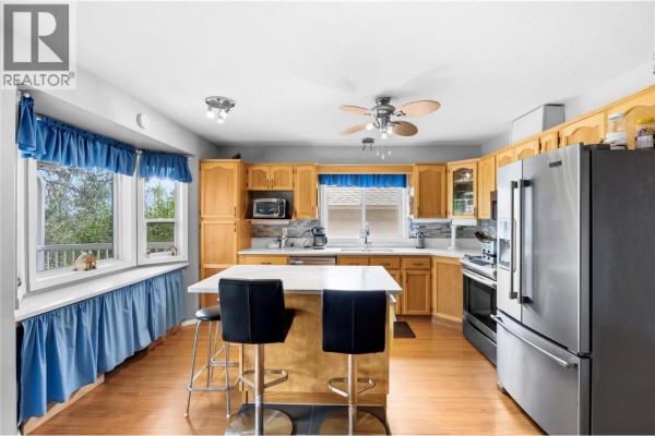 Kitchen with light wood cabinets, stainless steel appliances, a large island with bar stools, and a window view. - 1634 Carmi Avenue Unit# 121, Penticton