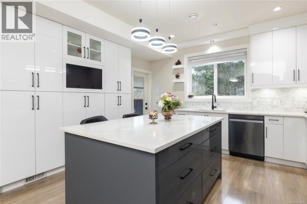Spacious white kitchen with dark grey island, stainless steel appliances, and large window. - 1636 Roberta Rd S, Nanaimo