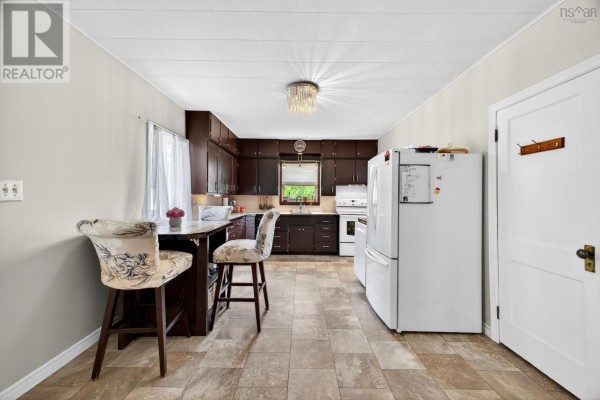 Kitchen with dark wood cabinets, a white refrigerator, a small dining table, and a doorway. - 16364 Highway 2, Springhill Junction