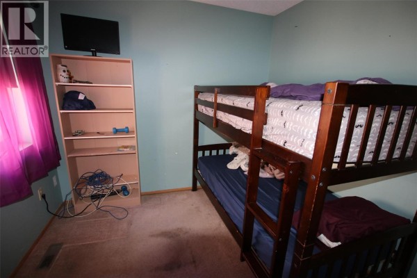 Bedroom with bunk beds, a bookshelf, and a window with purple curtains. - 164 Bergeron Drive, Tumbler Ridge