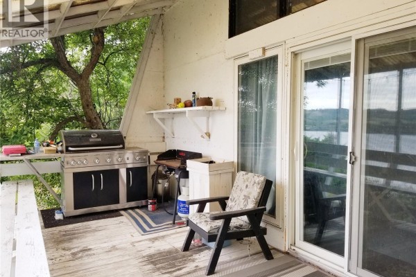Corner with a wood-burning stove, stacked cushions, and various wall decor. - 164 Garwell Drive, Buffalo Pound Lake