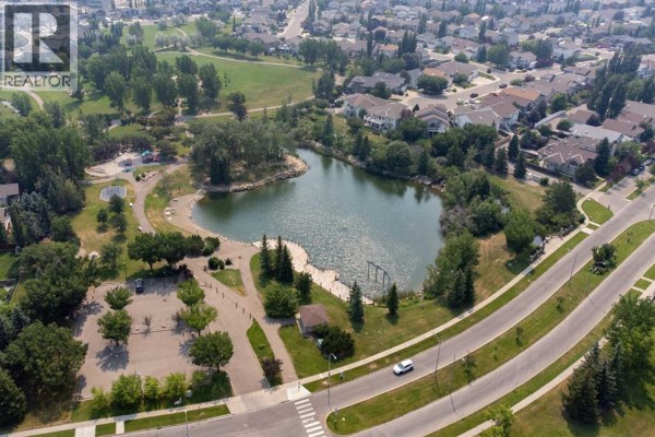 Aerial view of a pond and park area with walking paths and trees. - 164 Rivermill Landing W, Lethbridge