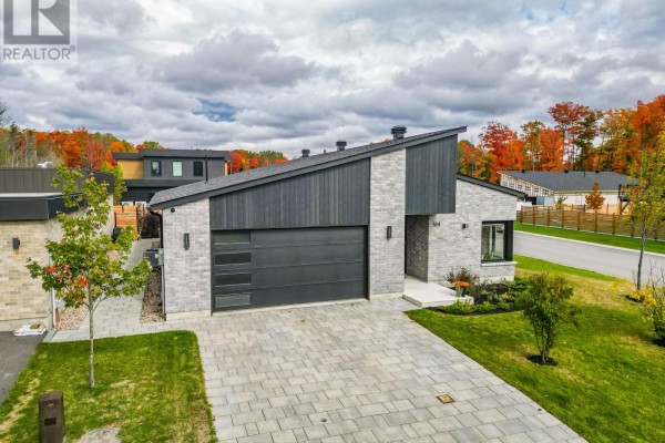 Front exterior of a modern house with light grey stone, dark wood accents, a black garage door, and a paved driveway. - 164 Sugarbush Street, North Bay