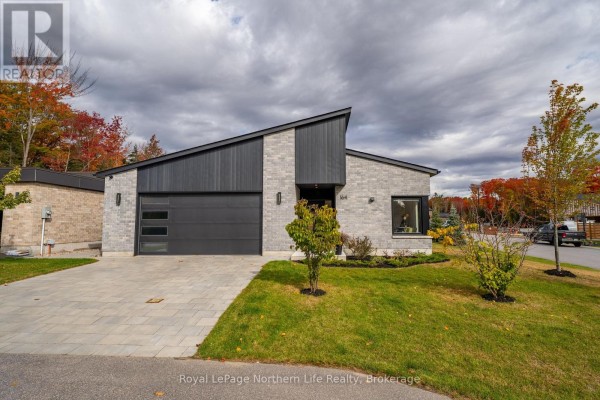 Front view of a contemporary house with a geometric roofline, stone and wood facade, green lawn, and mature trees. - 164 Sugarbush Street, North Bay
