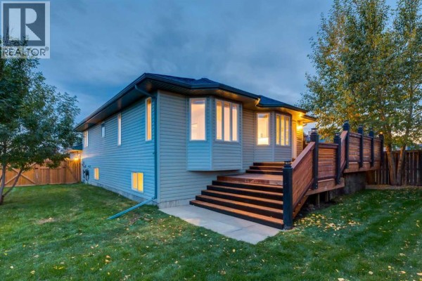 Rear exterior of the house with a wooden deck and stairs leading to the backyard. - 164 Sunset Heights, Crossfield