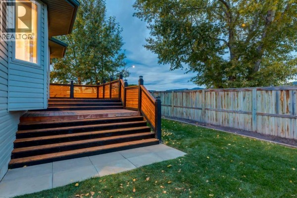 View of the wooden deck and backyard fence from the side of the house. - 164 Sunset Heights, Crossfield