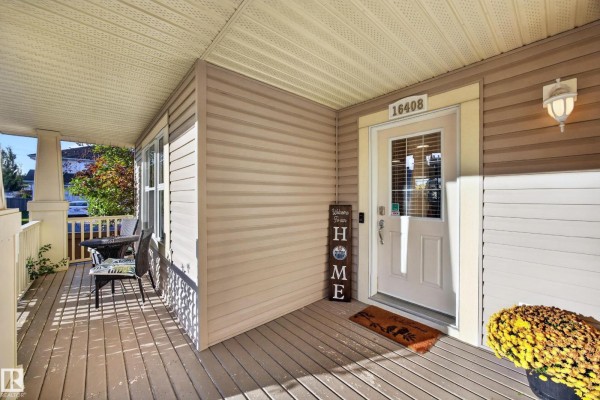 Covered front porch with two chairs, a table, and the front door with the house number. - 16408 59 St Nw, Edmonton