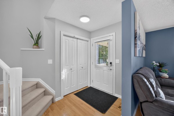 Foyer with beige laminate flooring, a white closet, and a carpeted staircase with white railing. - 16408 59 St Nw, Edmonton