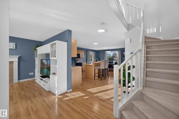 Open-concept living area with a blue accent wall, media unit, kitchen island, and stairs. - 16408 59 St Nw, Edmonton
