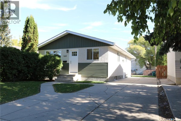 Front and side exterior view of a light-colored house with dark green trim and a paved driveway. - 1641 Thompson Avenue, Saskatoon