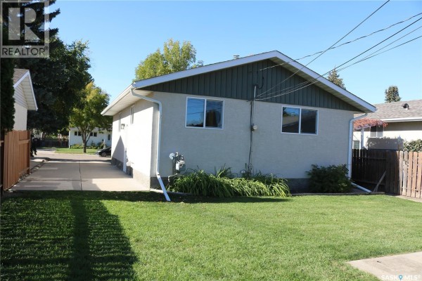 Rear exterior view of a light-colored house with a green lawn and a wooden fence. - 1641 Thompson Avenue, Saskatoon