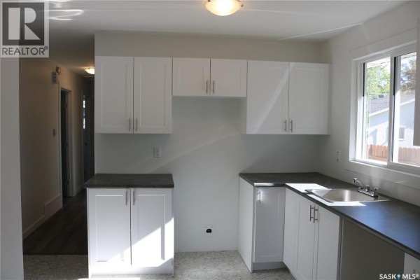 Kitchen with white cabinets, dark countertops, a stainless steel sink, and a window. - 1641 Thompson Avenue, Saskatoon