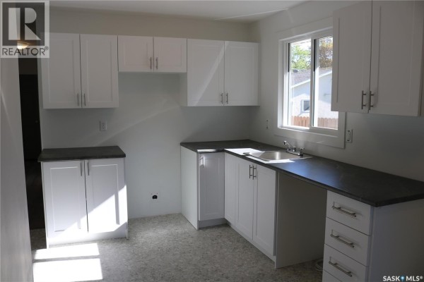 Kitchen with white cabinets, dark countertops, a stainless steel sink, and a window overlooking the backyard. - 1641 Thompson Avenue, Saskatoon