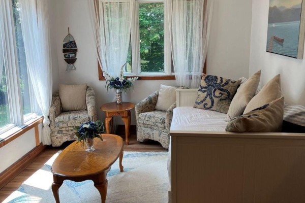 Sunroom with two armchairs, a daybed, and a coffee table with lake-themed decor. - 16431 Hwy 35, Algonquin Highlands