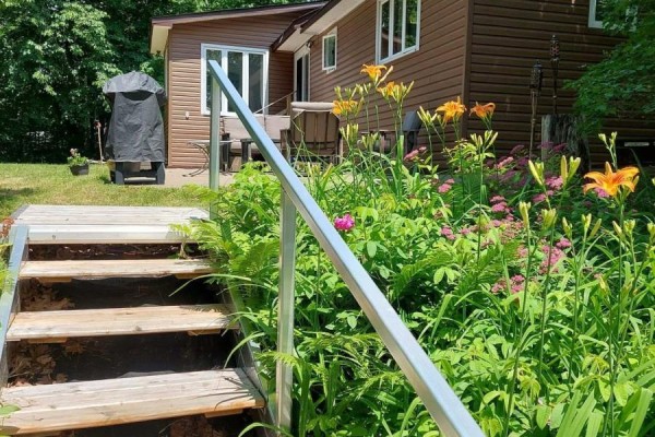 Wooden stairs with metal railings leading down into a garden with flowering plants. - 16431 Hwy 35, Algonquin Highlands