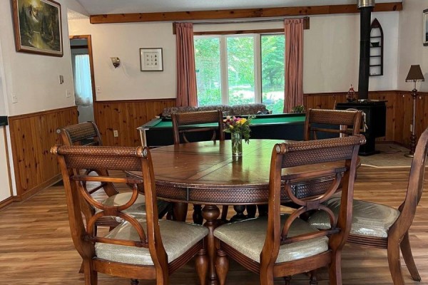 Dining room with a round wooden table, chairs, and a pool table in the background. - 16431 Hwy 35, Algonquin Highlands