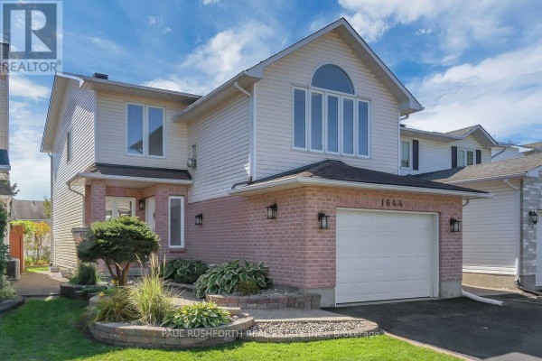 Side view of a two-story beige house with a brick lower level and attached garage. - 1644 Toulouse Crescent, Ottawa