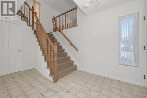 Interior staircase with tan carpet and wooden railings from the foyer with tile flooring. - 1644 Toulouse Crescent, Ottawa