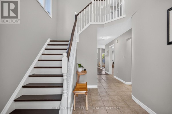 Interior foyer with a staircase featuring dark wood treads and white spindles, beige tile flooring. - 1647 Bayswater Crescent, London North