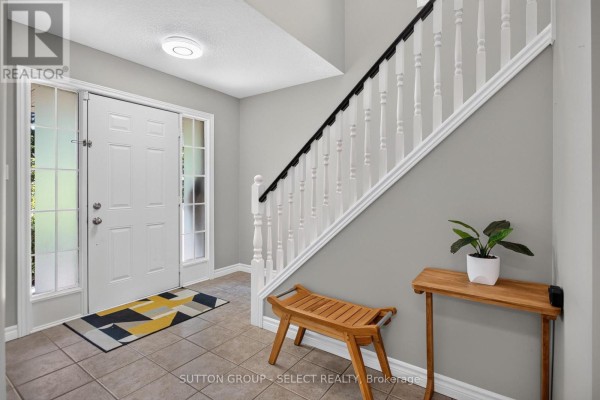 Entrance foyer with a white front door, frosted glass sidelights, tiled floor, and a wooden bench. - 1647 Bayswater Crescent, London North