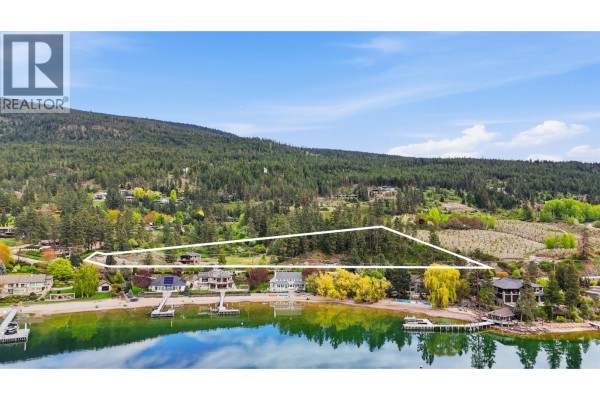 Aerial view of a house on a sloped, grassy lot with a driveway and wooded background. - 16475 Carrs Landing Road, Lake Country