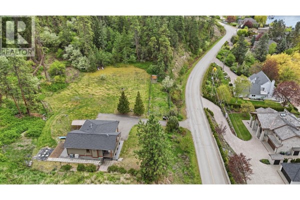 Exterior view of a multi-level house with wood and stone siding, deck, and grassy lawn. - 16475 Carrs Landing Road, Lake Country