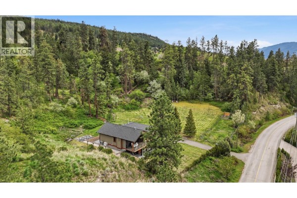 View from a covered deck with white patio furniture overlooking a lake and distant hills. - 16475 Carrs Landing Road, Lake Country