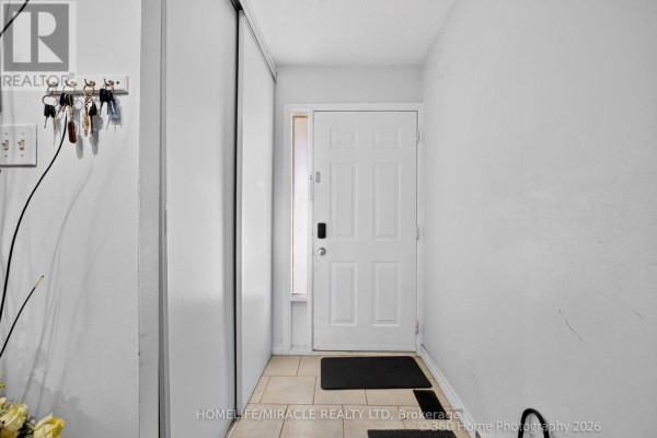 Interior view of a townhouse entrance with a white door, tiled floor, and coat rack. - 165 - 74 Springfair Avenue, Aurora