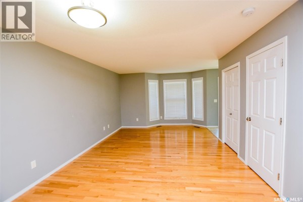 Empty living room with hardwood floors, grey walls, and a bay window. - 165 615 Stensrud Road, Saskatoon