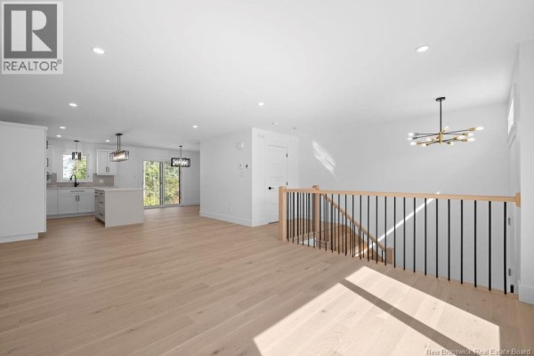 Living room area with light wood floors, white walls, and view of staircase with black spindles. - 165 Carrington Drive, Riverview