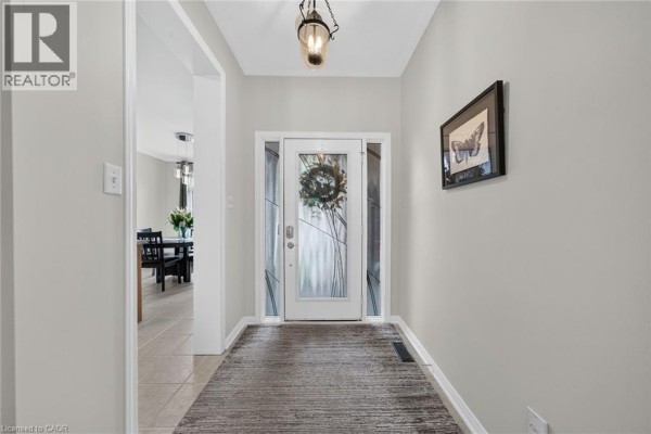 Interior view of a townhouse foyer with a glass front door, light grey walls, and a rug. - 165 Doon Mills Drive, Kitchener