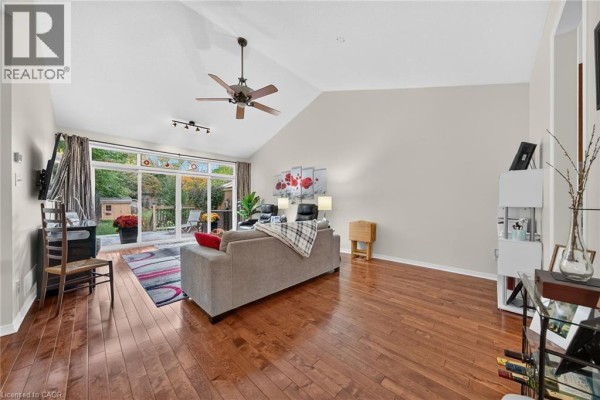 Living room with vaulted ceiling, hardwood floors, grey sofa, and sliding glass doors to a patio. - 165 Doon Mills Drive, Kitchener