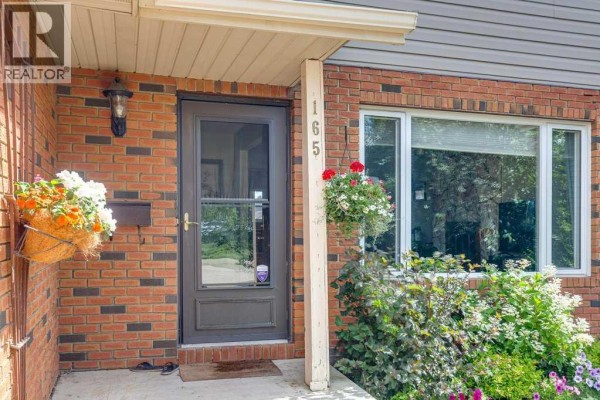 The front door area of the house, with brick facade, glass storm door, and hanging flower baskets. - 165 Greig Drive, Red Deer