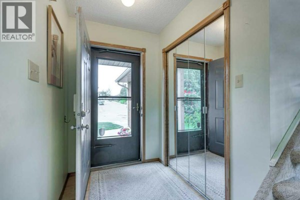 Interior view of a hallway showing the front door, a mirrored closet, and carpeted floor. - 165 Greig Drive, Red Deer