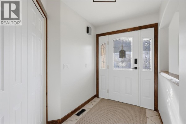 Interior view of a bright entryway with white walls, a tiled floor, and a wooden door frame. - 165 Hoovers Ferry Road, Kamloops