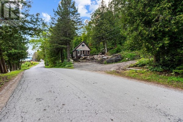 Street view of 165 Mallory Beach Road, a small home surrounded by trees and situated on a gravel driveway. - 165 Mallory Beach Road, South Bruce Peninsula