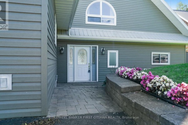 Front entrance of a grey home with a paved walkway and flowers. - 165 Rideau Street, Drummond/north Elmsley