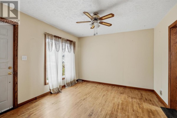 View of a living room with hardwood floors, a ceiling fan, and a large window. - 165 Spadina Ave, Sault Ste  Marie