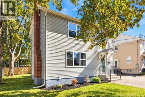 Side view of a gray house with a red brick chimney and white trim windows. - 165 West Lane, Moncton