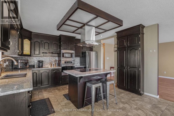 A dark wood kitchen with granite countertops, stainless steel appliances, and a central island with a stovetop. - 1658 600 Route W, The Nation