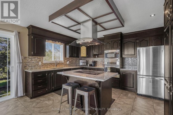 A dark wood kitchen with granite countertops, tile backsplash, and a window overlooking the yard. - 1658 600 Route W, The Nation