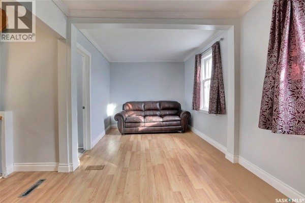 Interior view of a living room showing a brown leather sofa and wood floors, with a view into an adjacent hallway. - 1659 Montreal Street, Regina