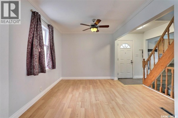 Living room with light blue walls, wood floors, a ceiling fan, and a view of the front door and staircase. - 1659 Montreal Street, Regina